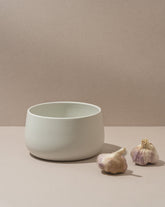 A person is serving salad from a black stoneware serving bowl on a dining table, with a white plate and a glass of white wine in the background.